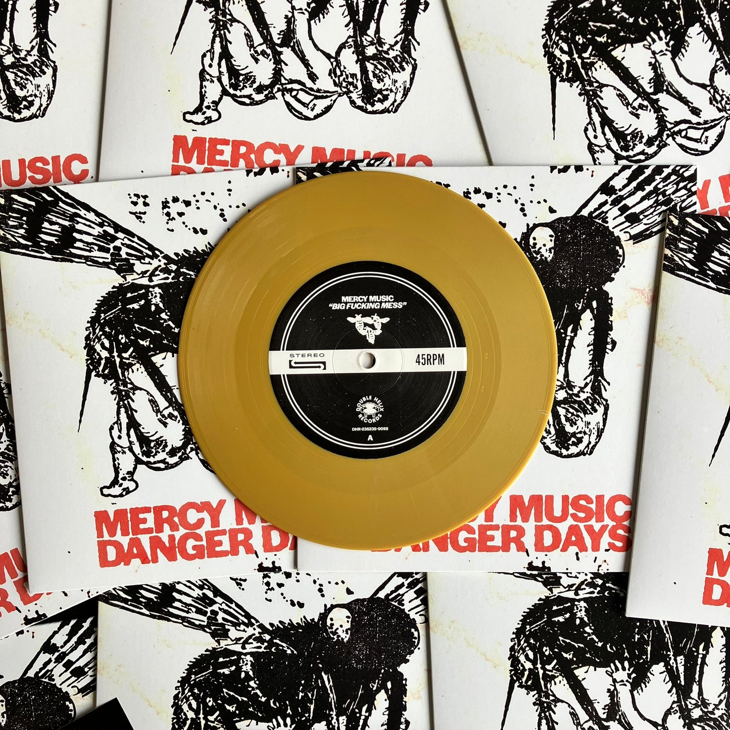 Gold vinyl record with a black label on top of 'Mercy Music' album covers.