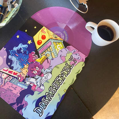 Colorful vinyl record with 'Disassembly' text on a desk with a laptop and coffee cup.