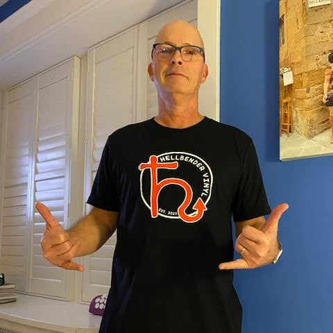 Man wearing a black t-shirt with a logo, giving a thumbs-up gesture indoors.