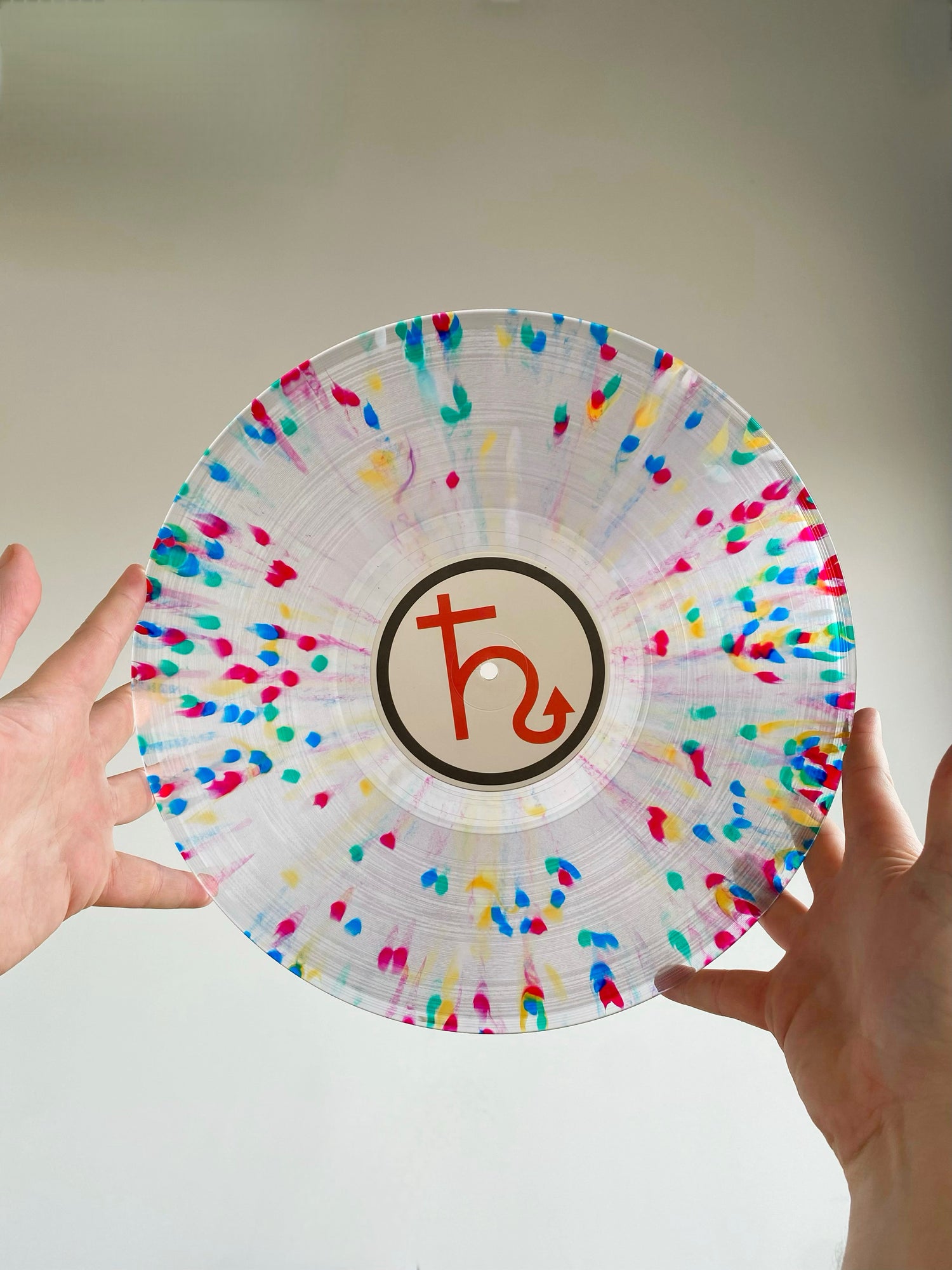 Hands holding a custom-pressed vinyl record with colorful splatter design from Hellbender Vinyl