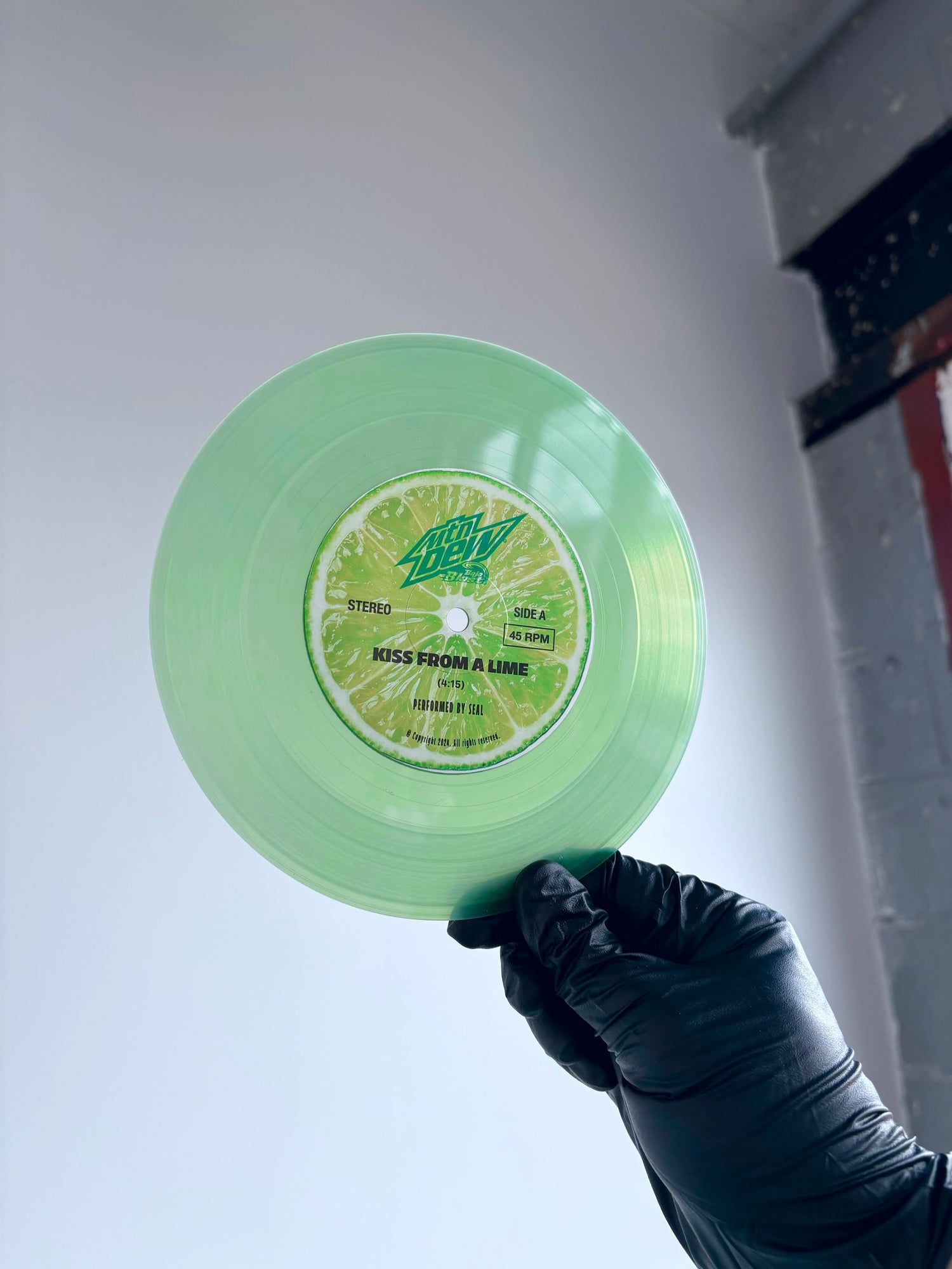 Hand in black glove holding green Mountain Dew vinyl record by Seal for corporate sales