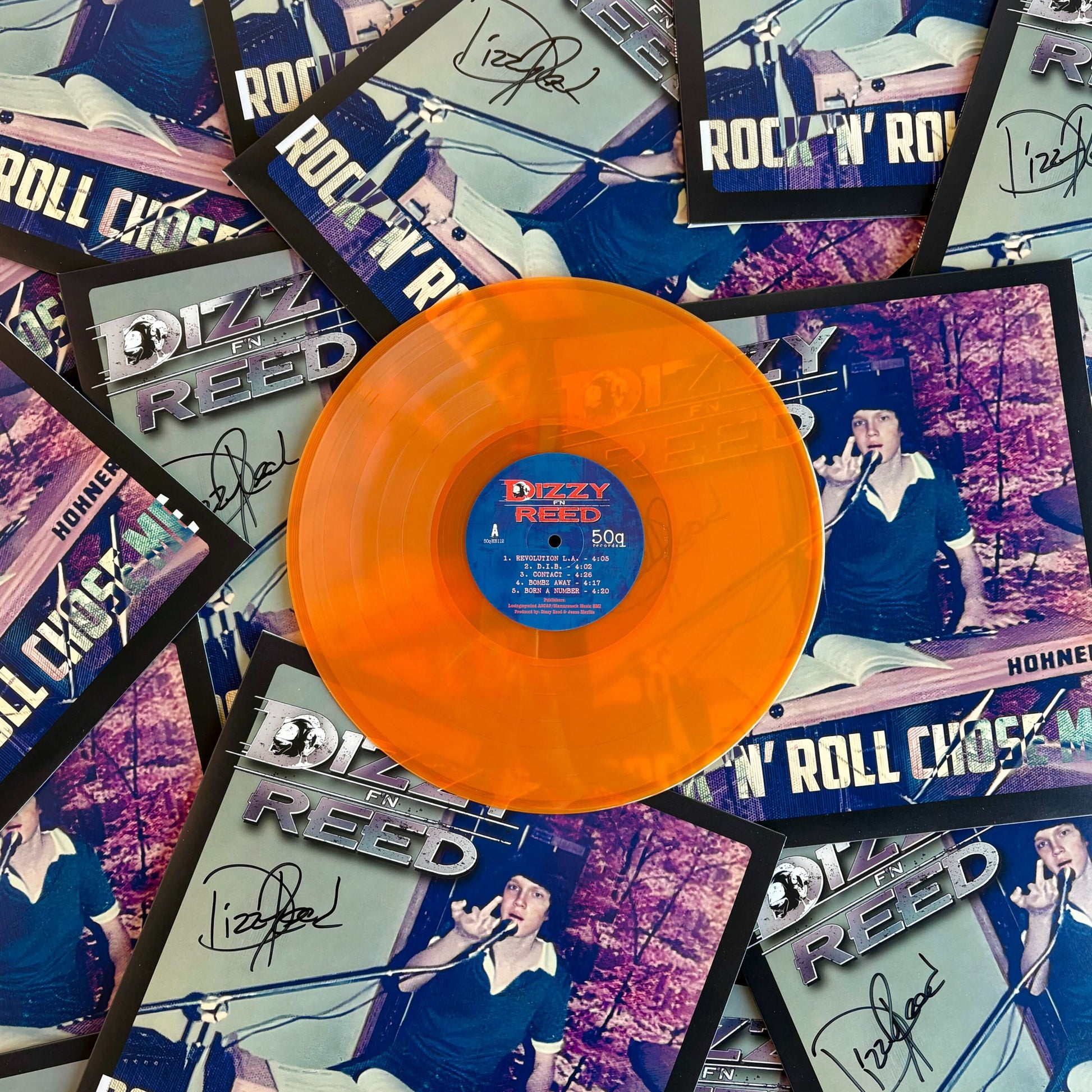 Hazy orange vinyl record with a blue label on top of Dizzy Reed album covers