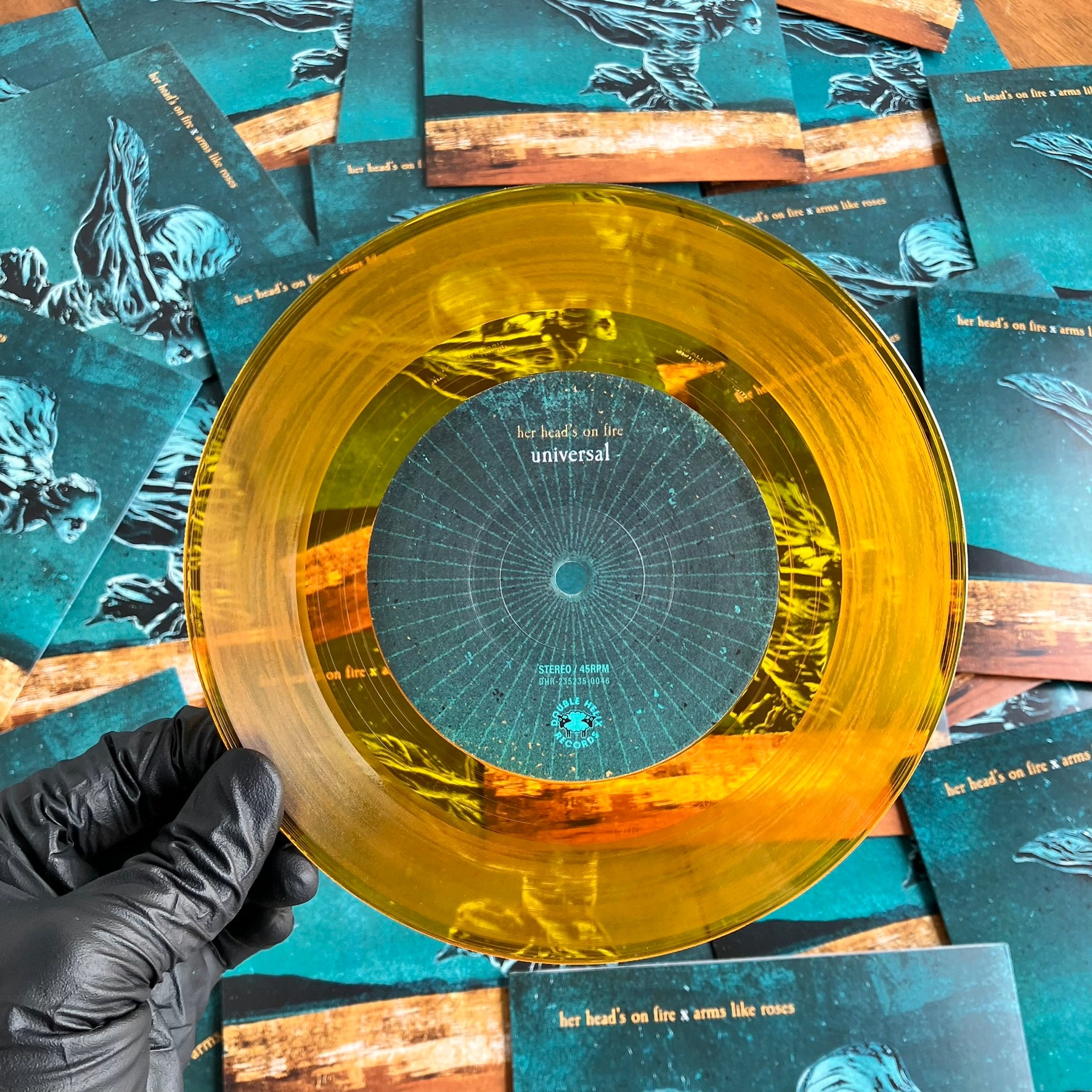 Clear orange vinyl record held by a gloved hand with album covers in the background